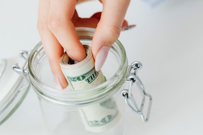 Hand placing rolled dollar bills into a glass savings jar